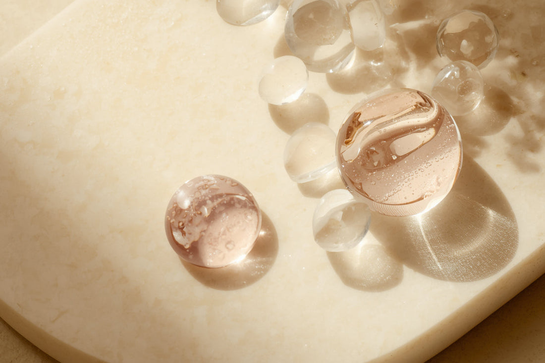 Translucent glass beads and serum-like textures on warm ivory stone for a peptide-ingredient article.